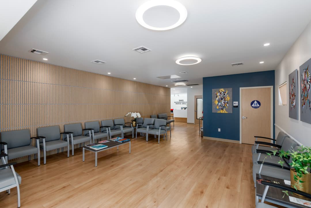 Modern waiting room with gray chairs, wooden flooring, and colorful artwork on the walls.