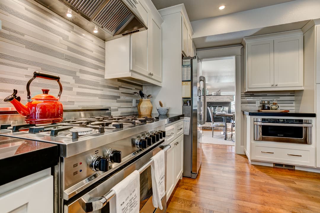 Modern kitchen with stainless steel appliances, red kettle, and stylish backsplash.