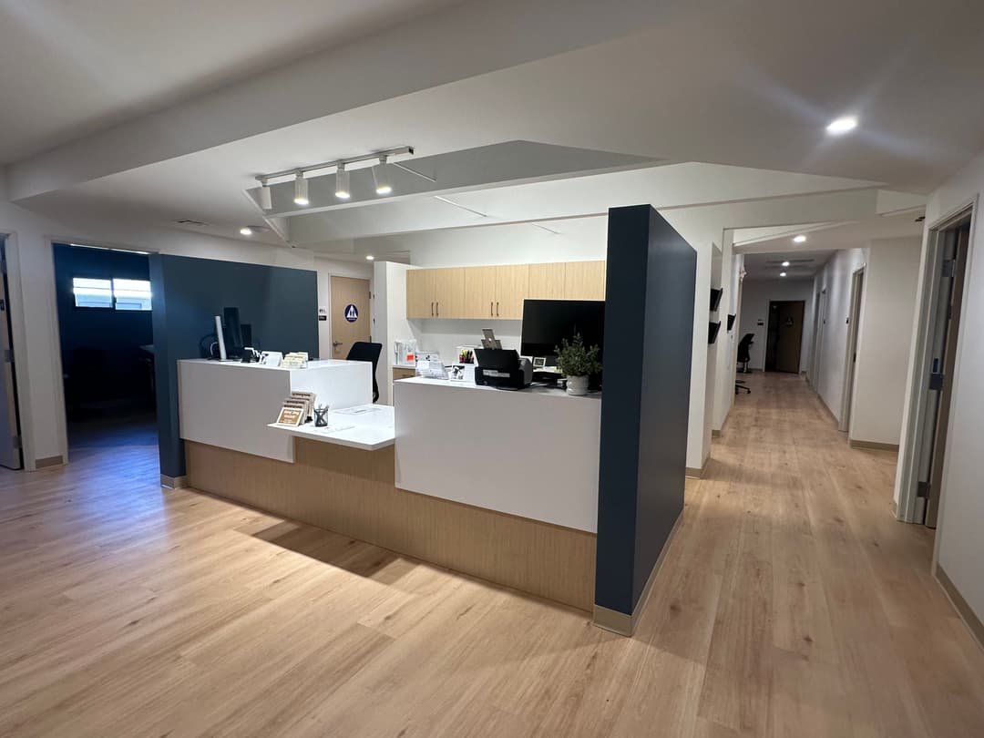 Modern office reception area with wooden flooring, desks, and contemporary design elements.