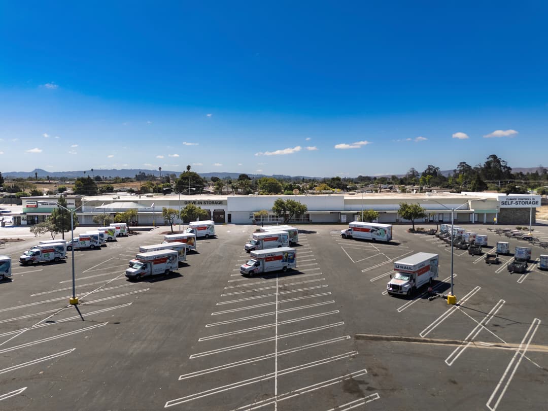 Aerial view of a parking lot with multiple moving trucks and storage buildings under a clear blue sky.