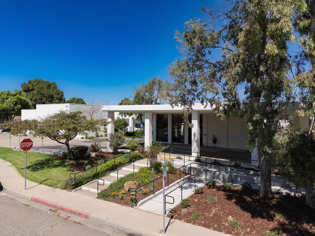 Modern building exterior with landscaped garden, blue sky, and a stop sign.