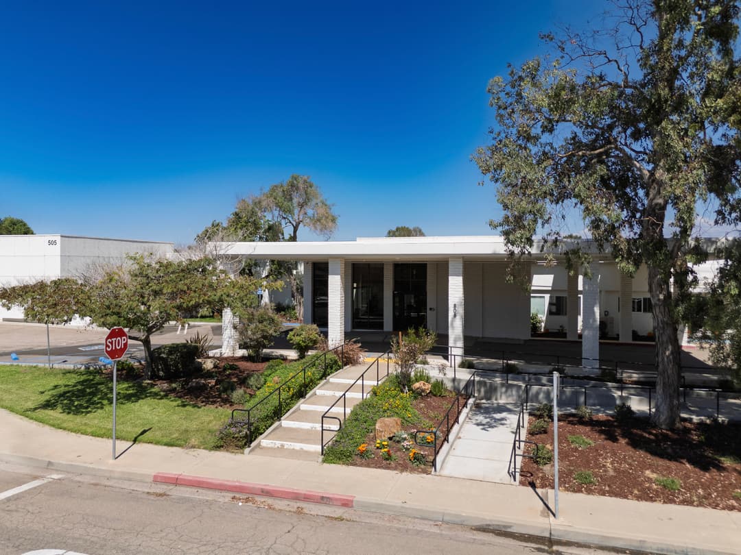 Modern building entrance with landscaped garden and stop sign on a sunny day.