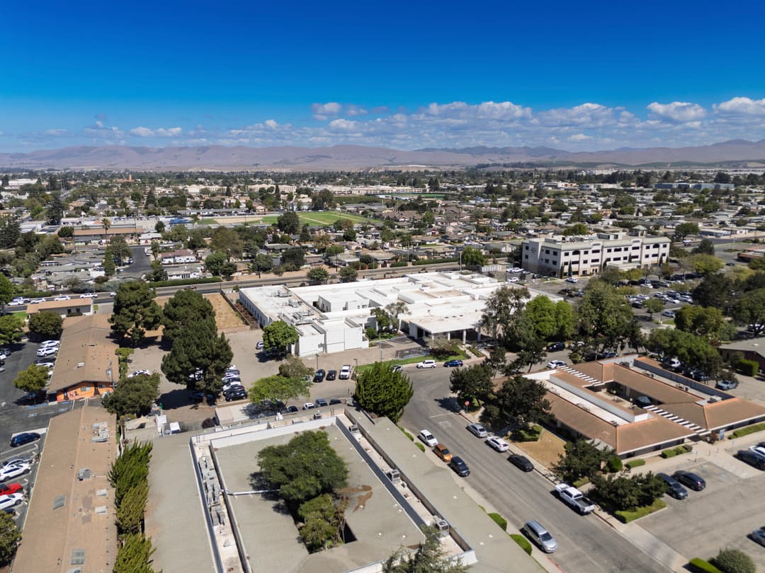 Aerial view of a suburban area with buildings, trees, and parking lots under a clear blue sky.