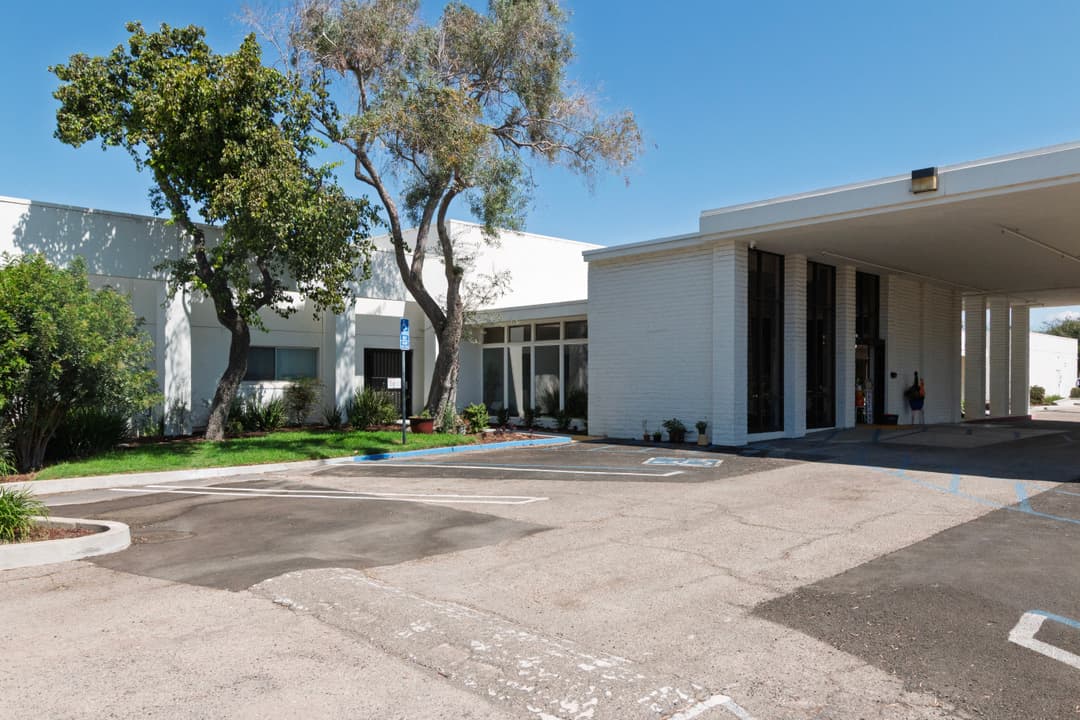 Modern building exterior with parking area and trees under a clear blue sky.
