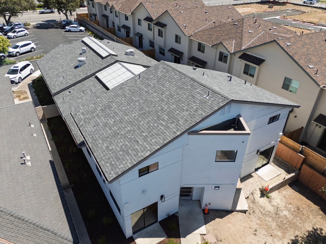 Aerial view of modern residential buildings with gray roofs and solar panels.
