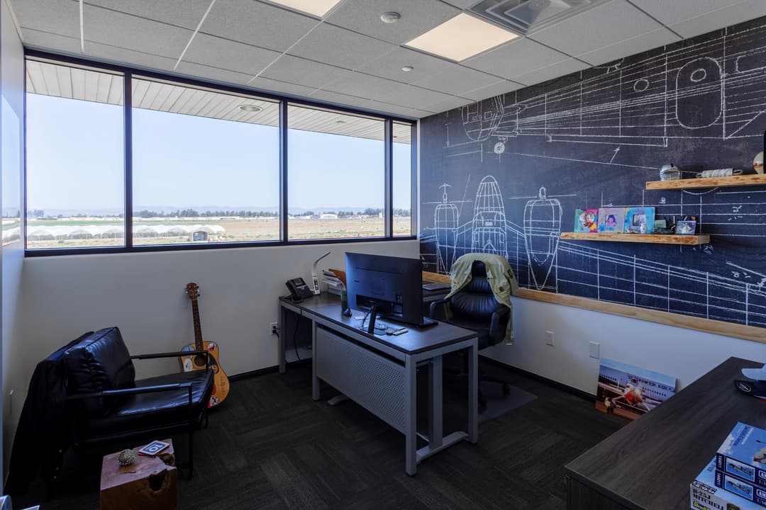 Modern office space with a large window, desk, and wall showcasing airplane blueprints.