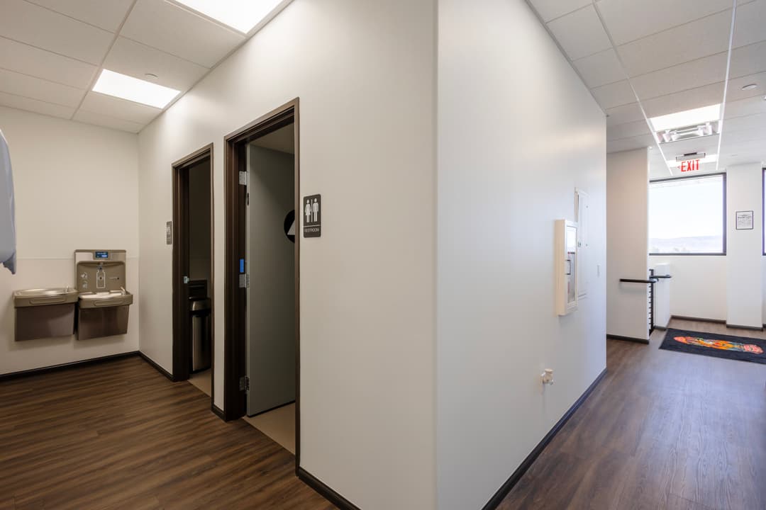 Modern office hallway featuring restrooms and water fountains in a well-lit environment.