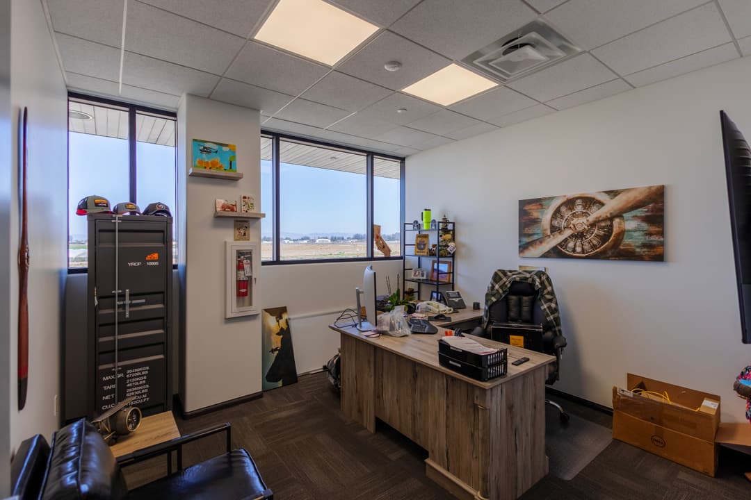 Modern office interior with a desk, ergonomic chair, large windows, and decorative wall art.