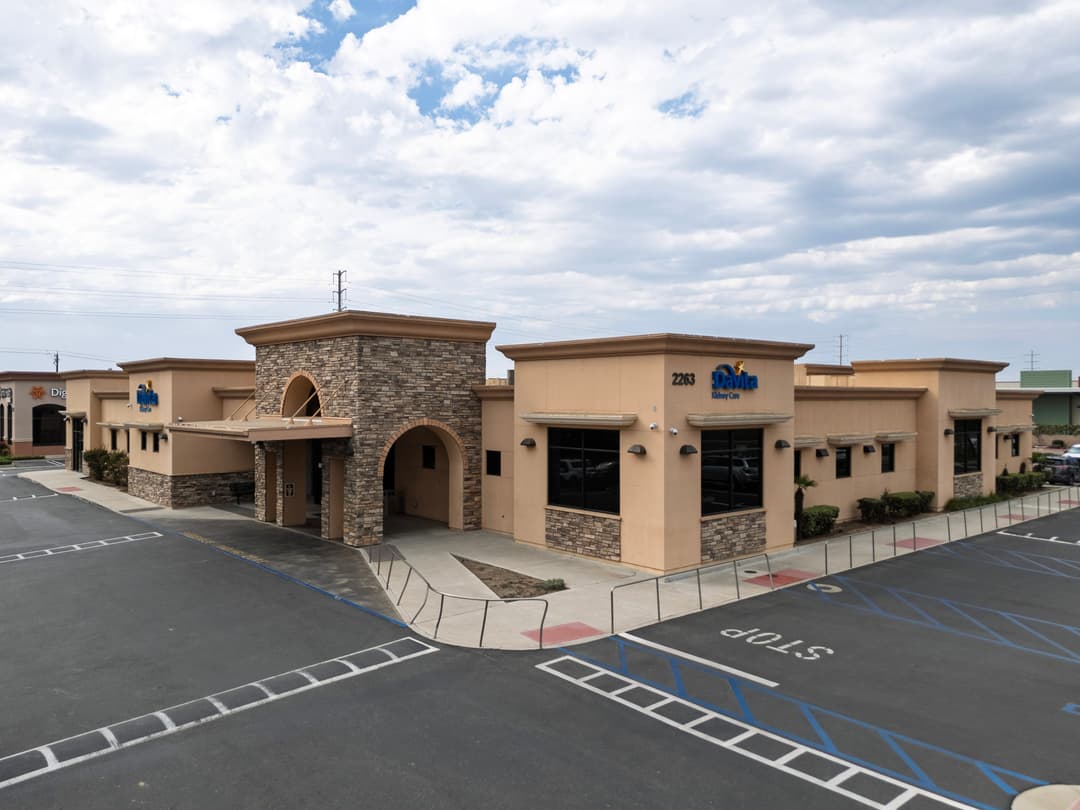 Modern stone-clad commercial building with large windows and parking lot.
