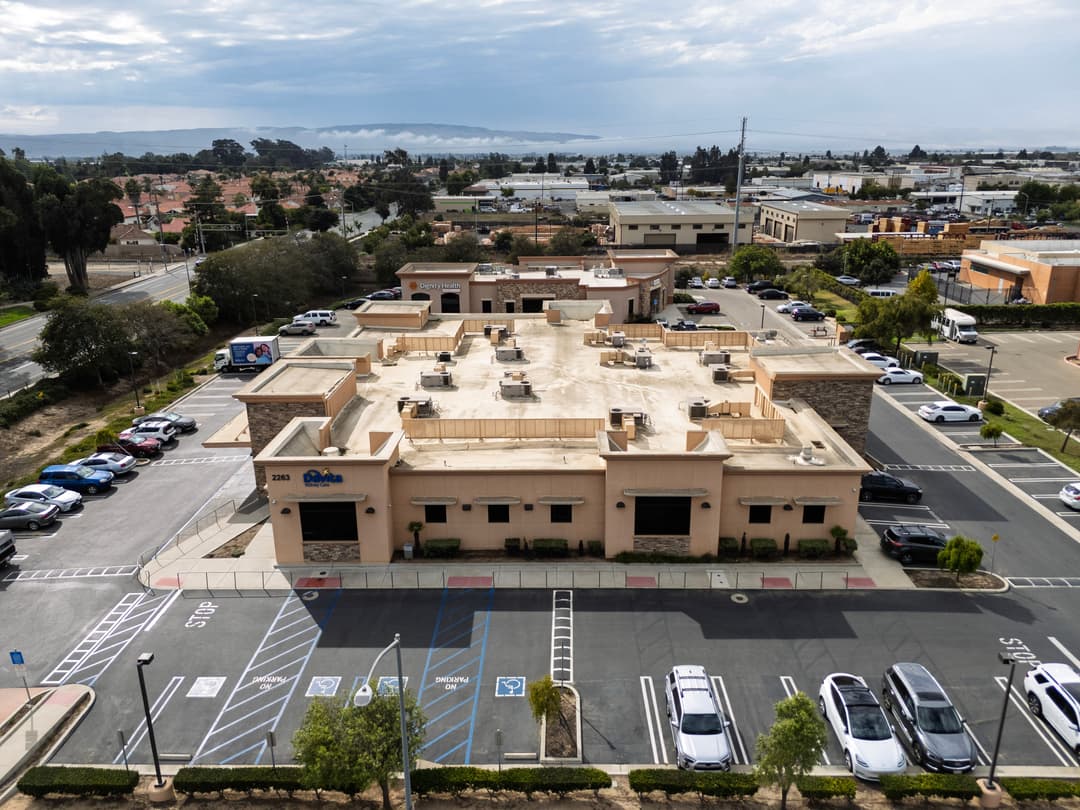 Aerial view of a commercial building with parking lot and coastal background.