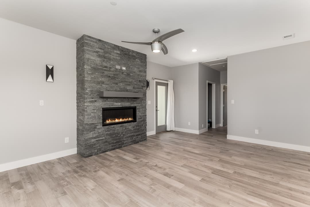 Modern living room featuring a stone fireplace, ceiling fan, and wood flooring.