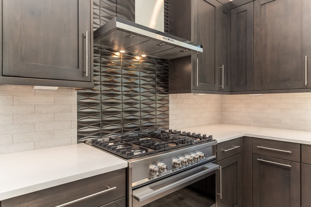 Modern kitchen with dark cabinetry, tile backsplash, and a stainless steel gas range.