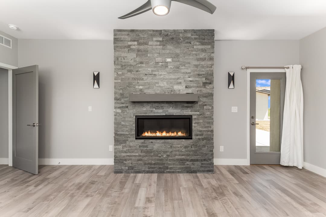 Modern living room with stone fireplace, light wood floors, and patio door.