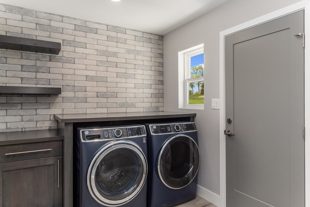 Modern laundry room with gray brick walls, high-efficiency washers, and a door leading outside.