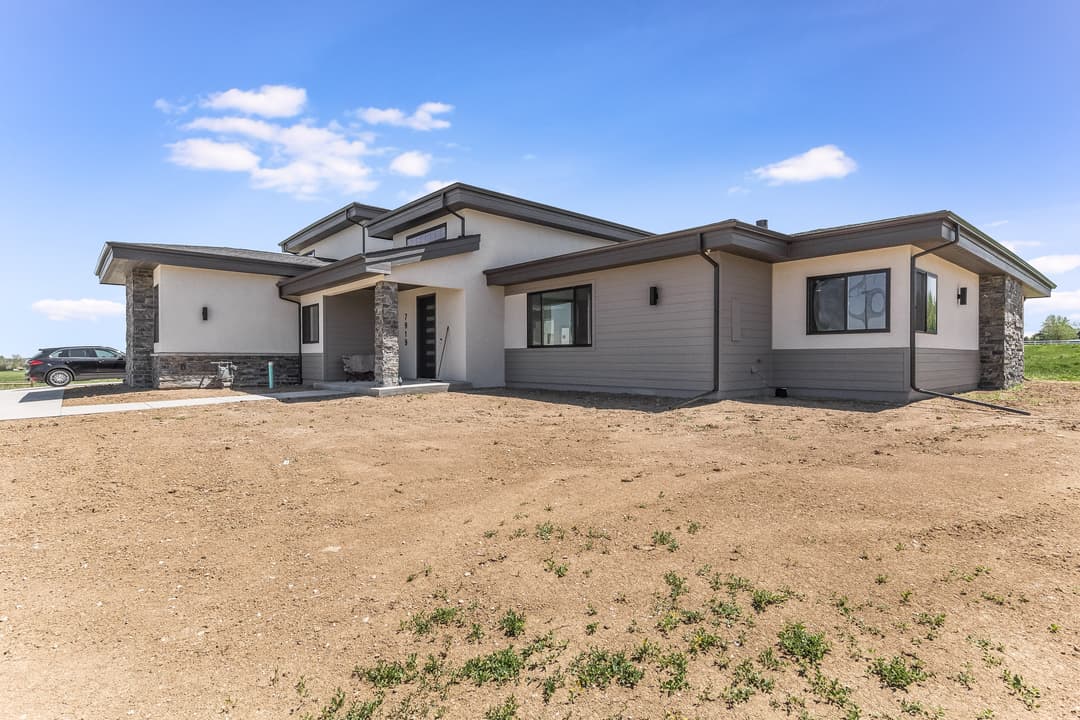 Modern single-story home with stone accents and a large yard under a blue sky.