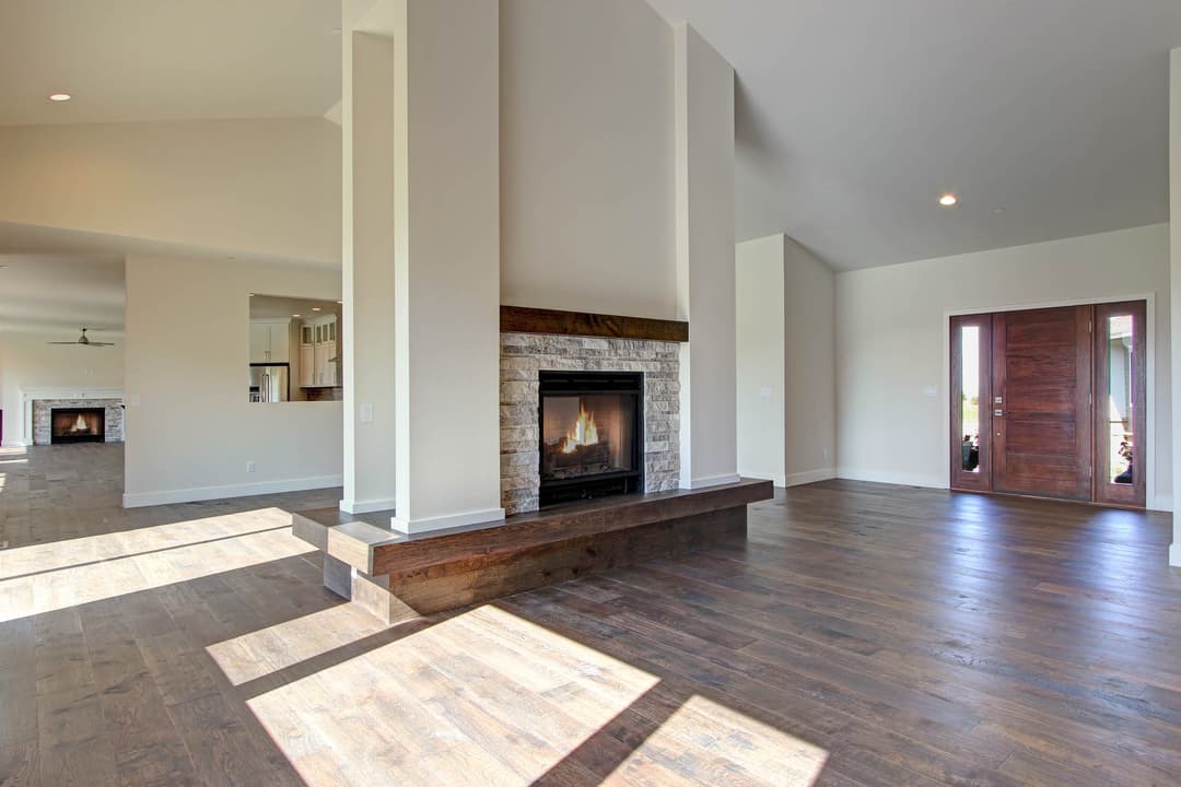 Modern living room with stone fireplace, hardwood floors, and open space design. Natural light in view.