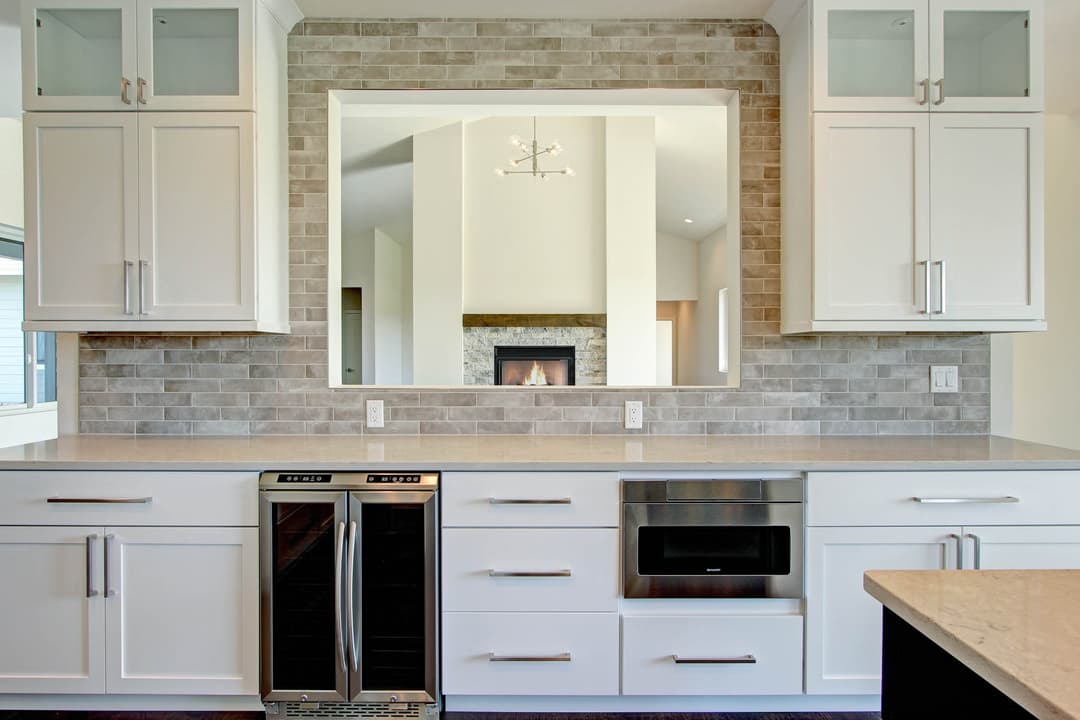 Modern kitchen with white cabinets, sleek appliances, and elegant grey tile backsplash.