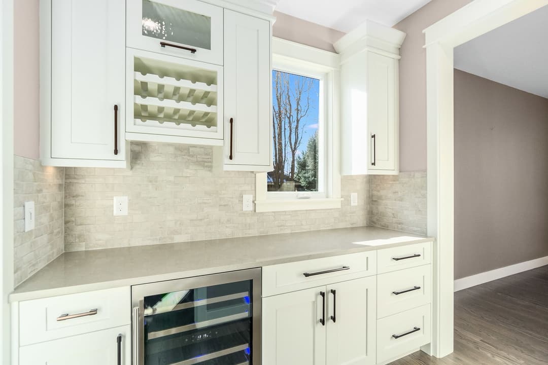 Modern kitchen with white cabinetry, stone backsplash, and built-in wine cooler. Natural light streaming in.
