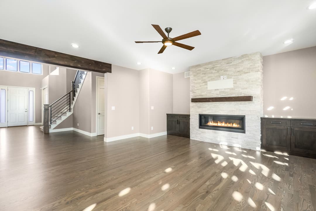 Spacious living room with modern fireplace, hardwood floors, and ceiling fan. Natural light streaming in.