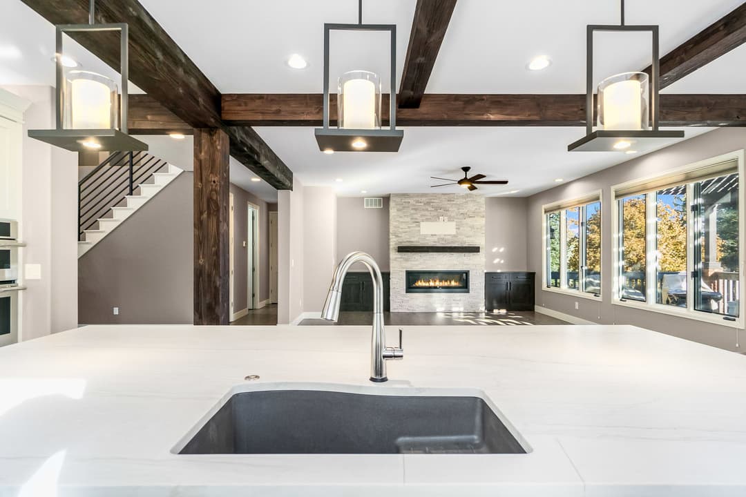 Modern kitchen with marble countertop, stylish pendant lights, and open living area with fireplace.