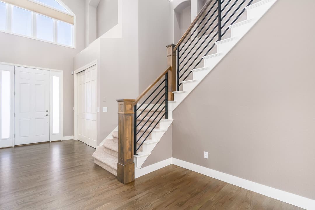 Bright entryway featuring a staircase with wooden railing and modern details, with light-colored walls.