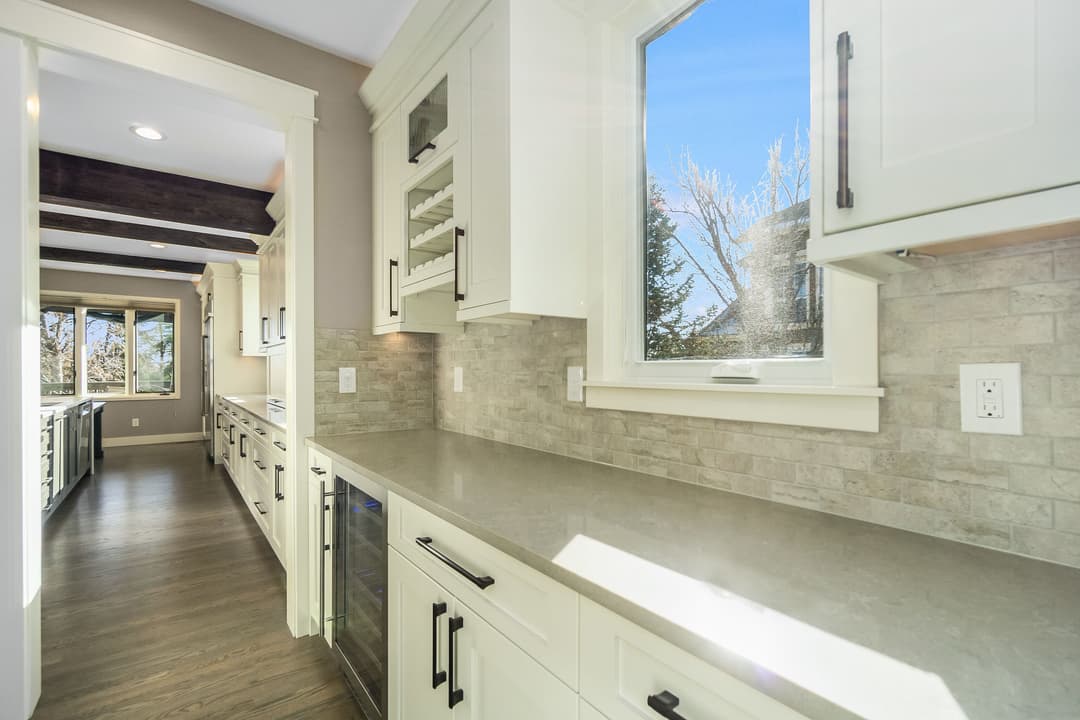 Modern kitchen interior featuring white cabinetry, gray countertops, and large windows.