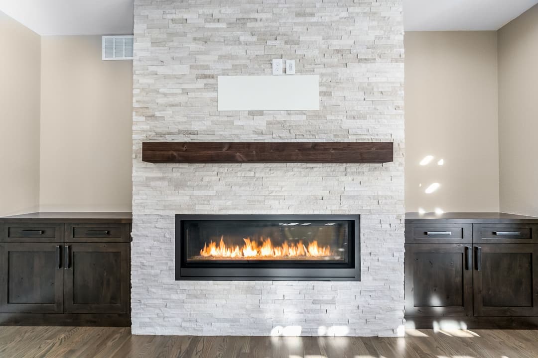 Modern living room with a stone fireplace, wooden mantel, and stylish cabinetry.
