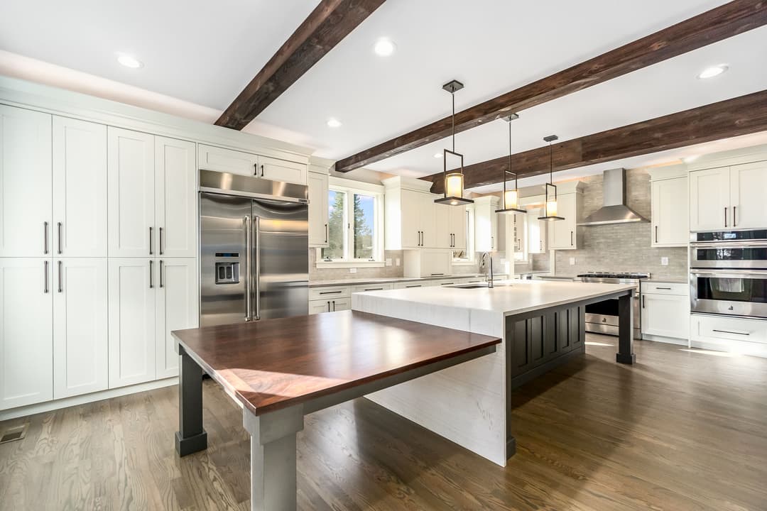 Modern kitchen with white cabinets, wooden beams, large island, and stainless steel appliances.