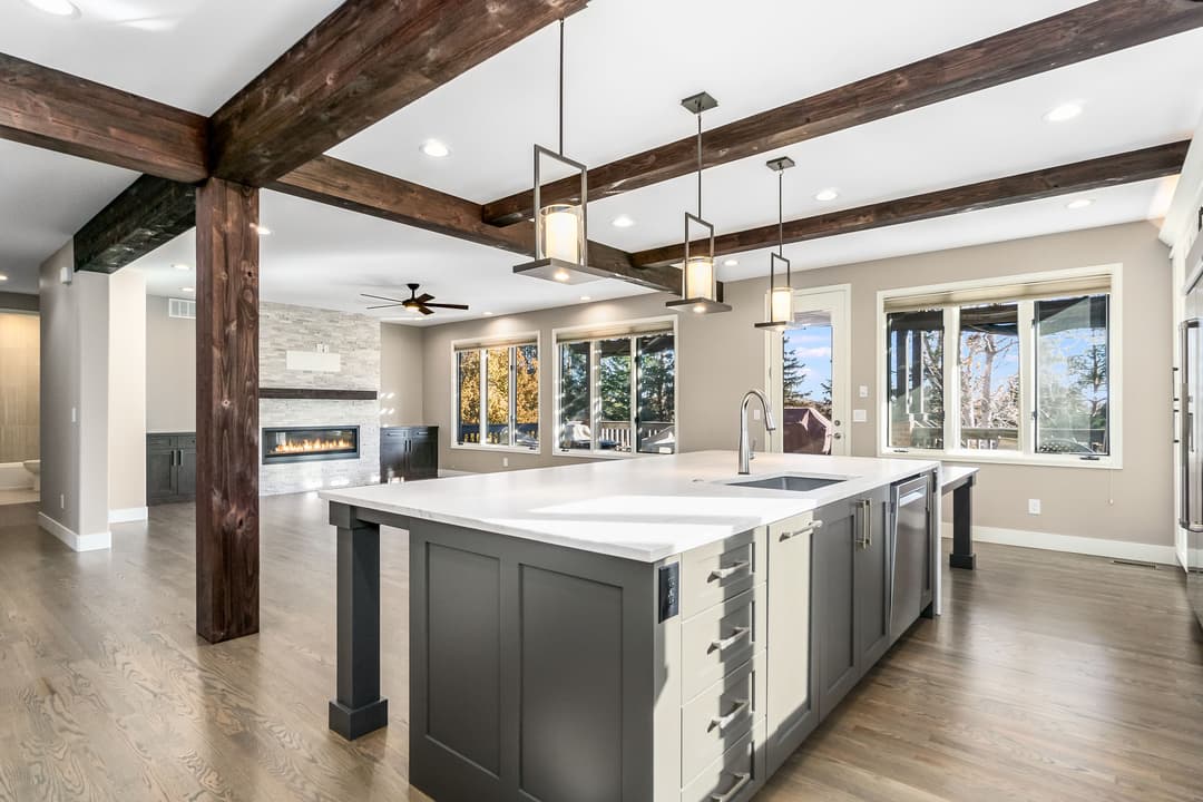 Modern kitchen with island, wooden beams, and large windows showcasing scenic views.