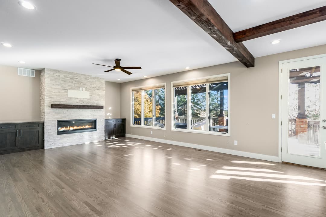 Spacious living room with stone fireplace, large windows, and wooden beam ceiling.