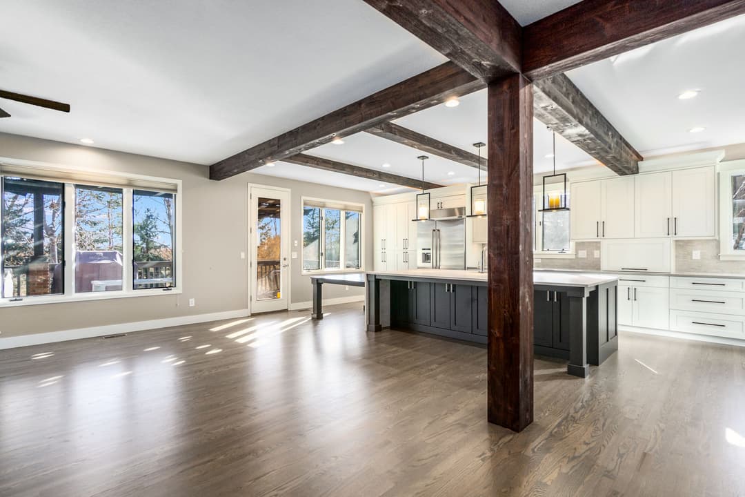 Modern kitchen with dark island, wooden beams, and large windows for natural light.