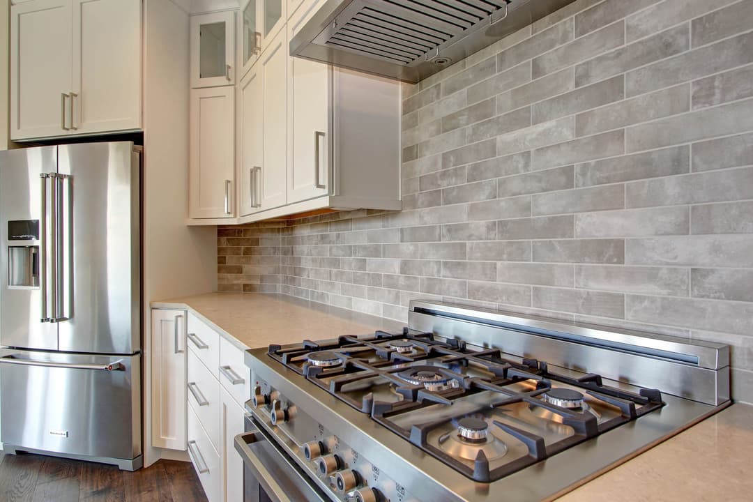 Modern kitchen featuring stainless steel appliances, a gas stove, and gray tiled backsplash.