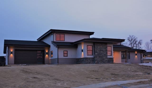 Modern two-story home with stone accents and glowing windows at dusk.