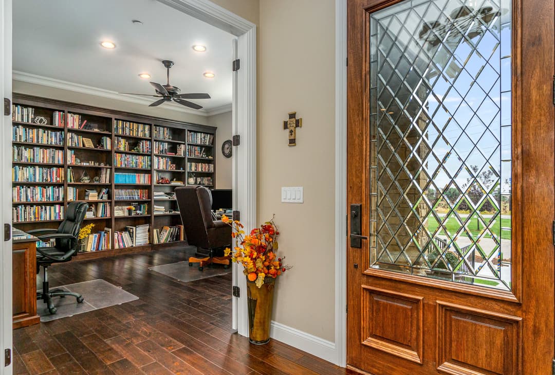 Welcoming entryway with a wooden door, bookshelf office, and decorative flower vase.