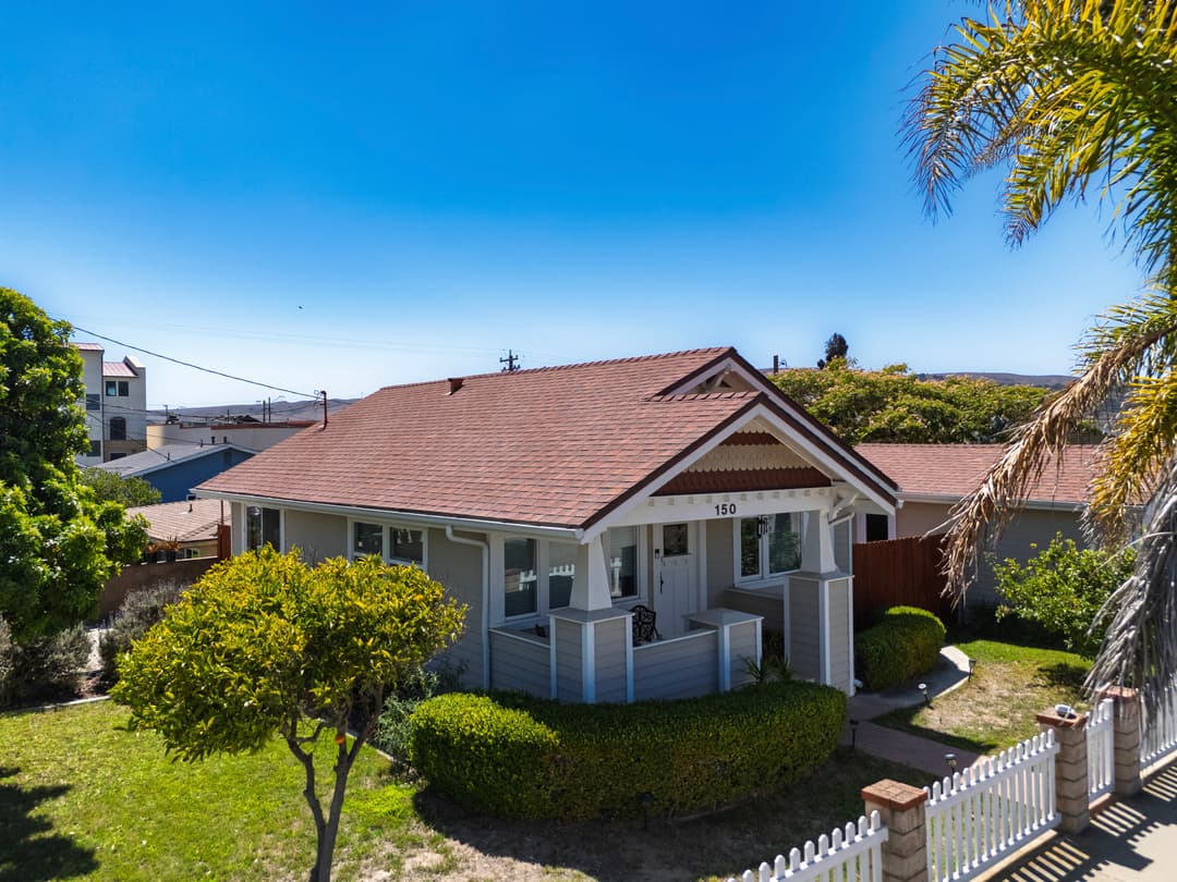 Charming single-story house with a red roof and lush front yard in sunny neighborhood.