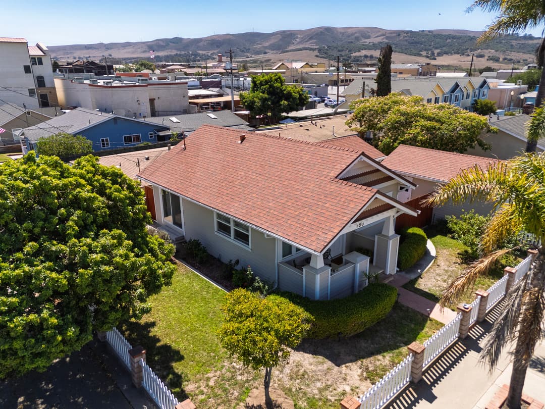 Aerial view of a single-story home with a red tile roof and landscaped yard in a coastal town.