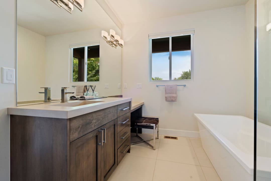 Modern bathroom with dual sinks, large mirror, and spacious tub, featuring natural light.