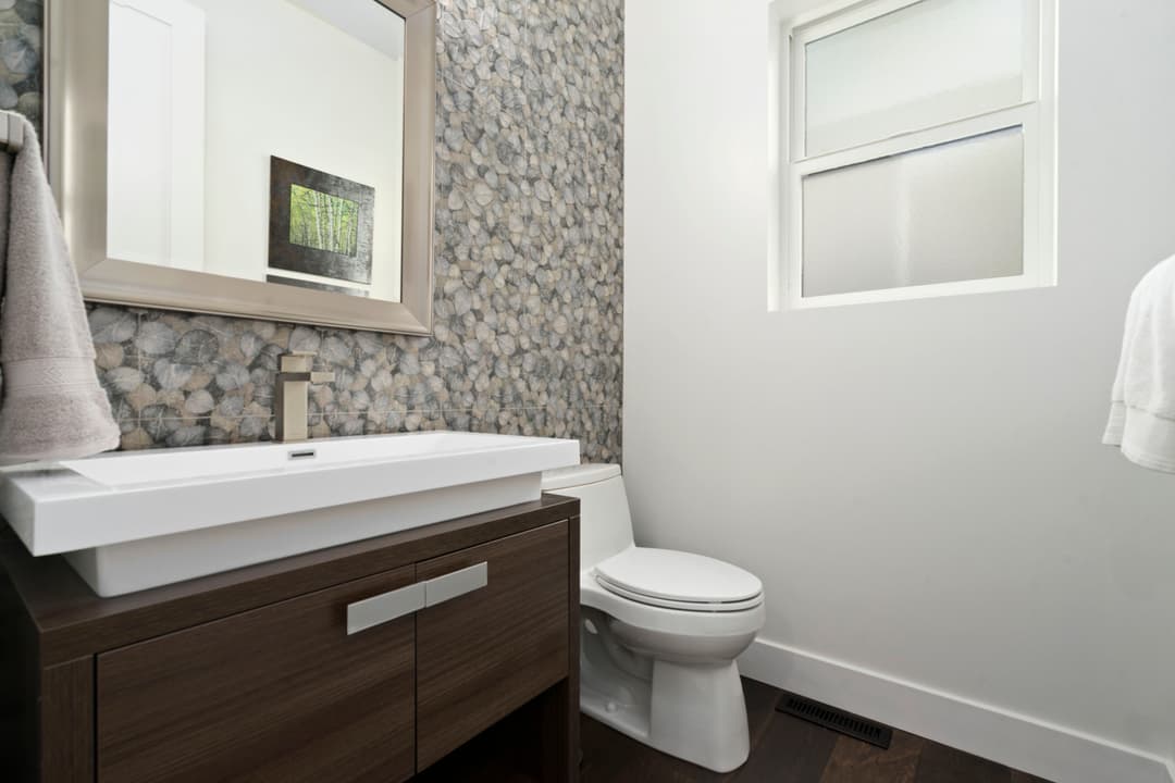 Modern bathroom featuring a sleek vanity, stone wall, and a toilet with natural lighting.