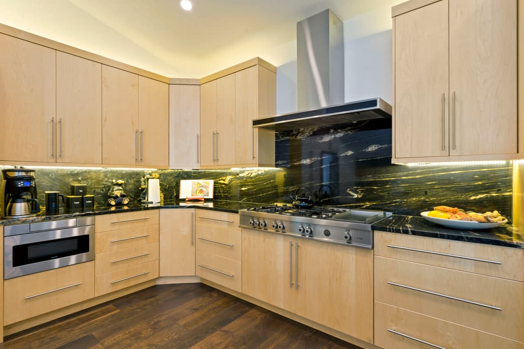 Modern kitchen with wood cabinets, stainless steel appliances, and sleek black marble backsplash.