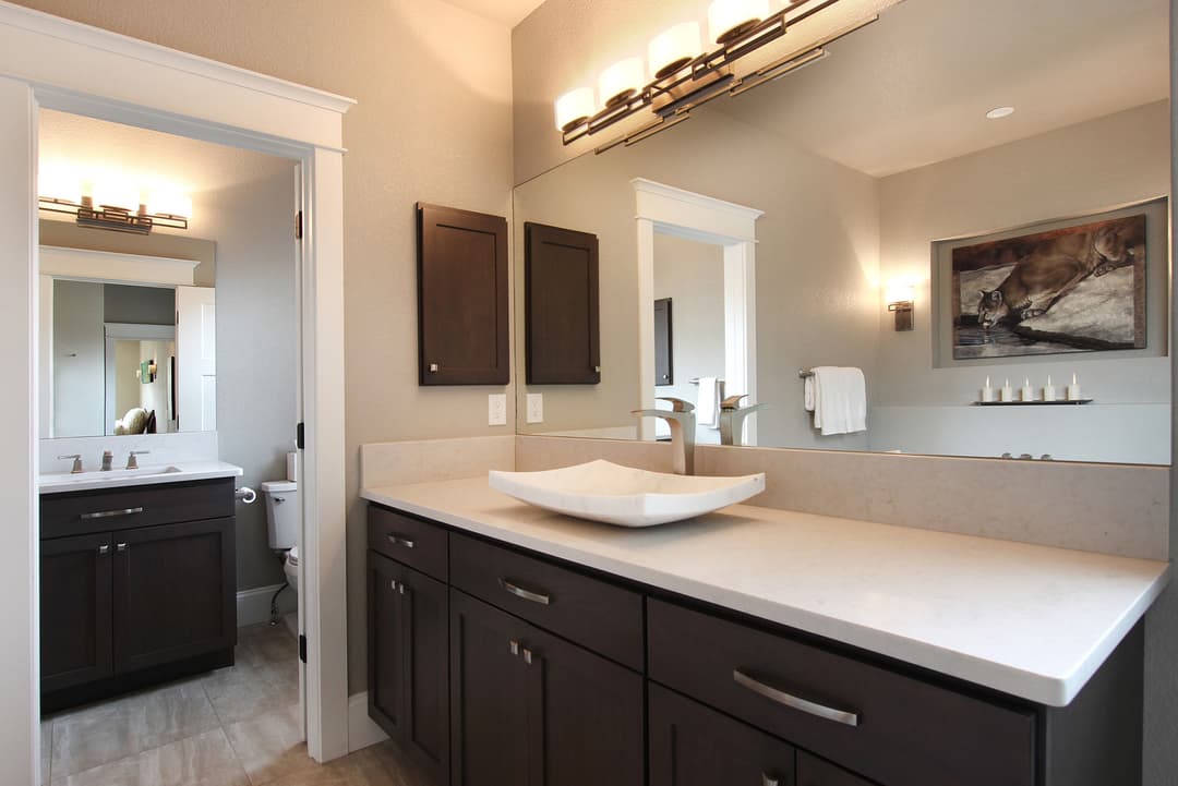 Modern bathroom with dark wood cabinets, sleek countertop, and illuminated mirrors.