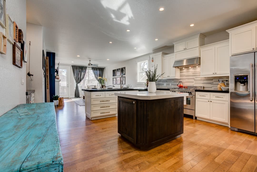 Modern kitchen with white cabinets, dark island, and hardwood floors, featuring natural light.