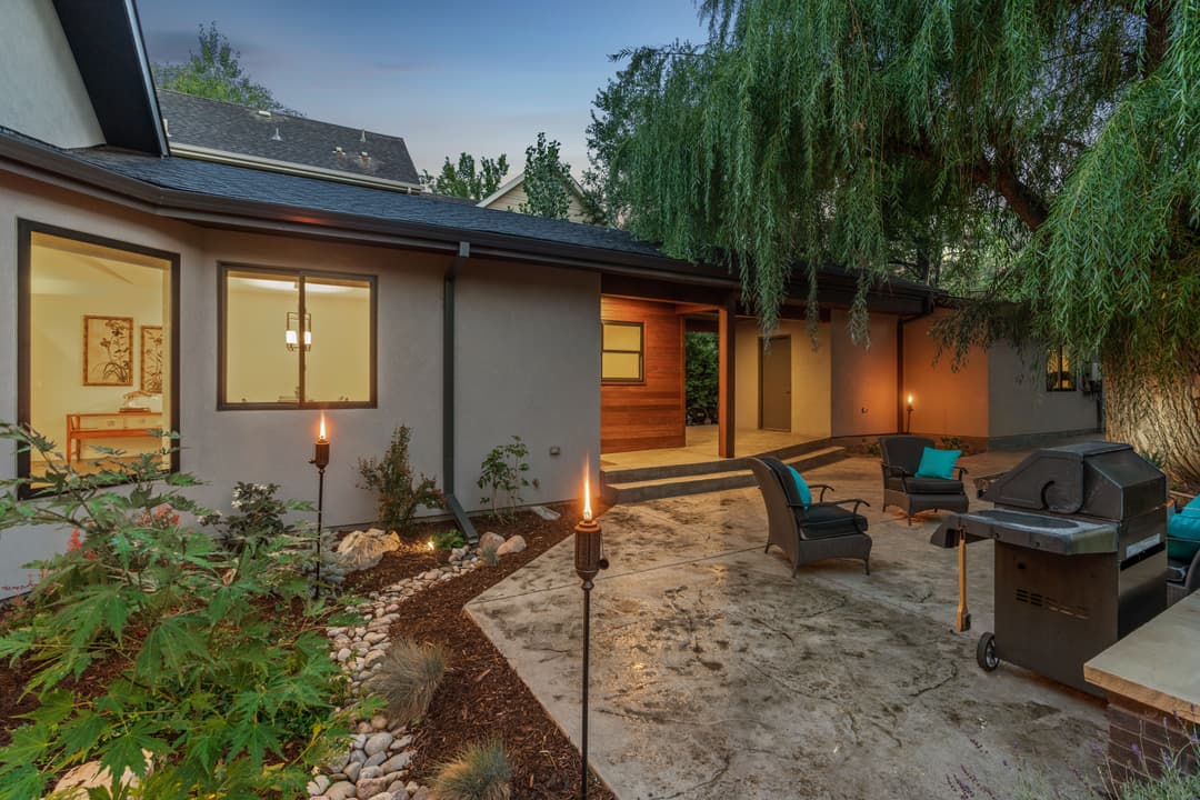 Cozy outdoor patio with grill, seating area, and landscaped garden in evening light.
