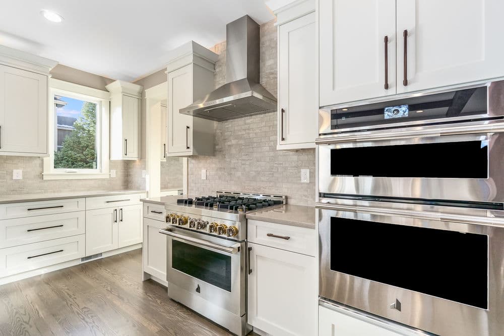 Modern kitchen with stainless steel appliances, white cabinetry, and sleek stone backsplash.