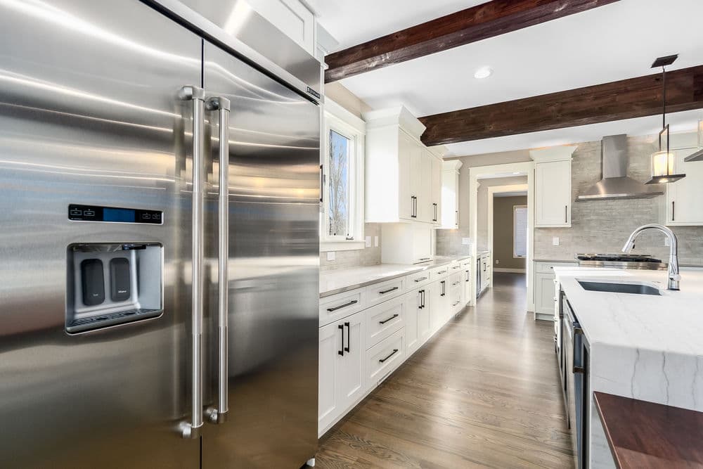 Modern kitchen with stainless steel appliances, marble countertops, and wooden beams.