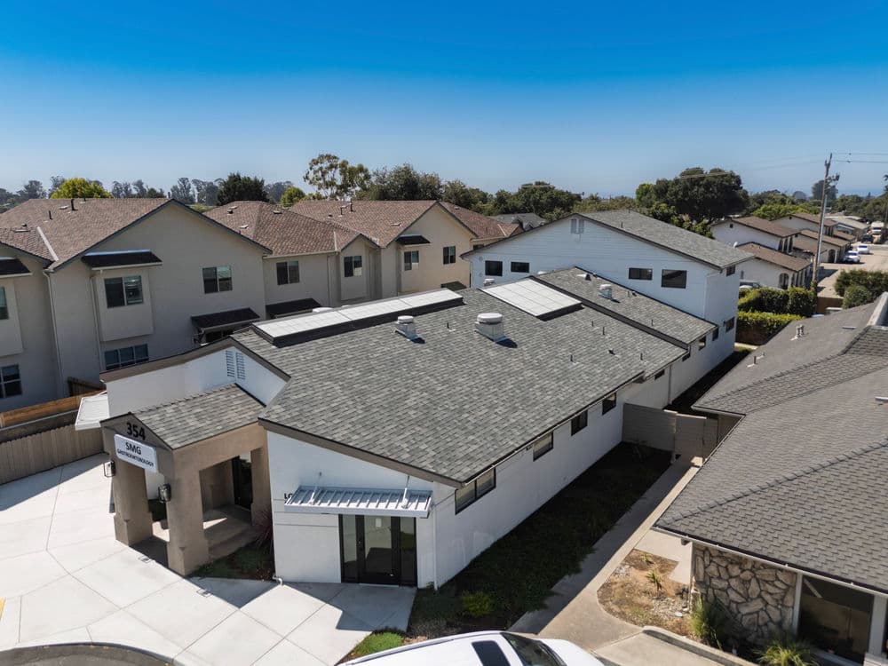 Aerial view of a modern building with solar panels, surrounded by residential homes.