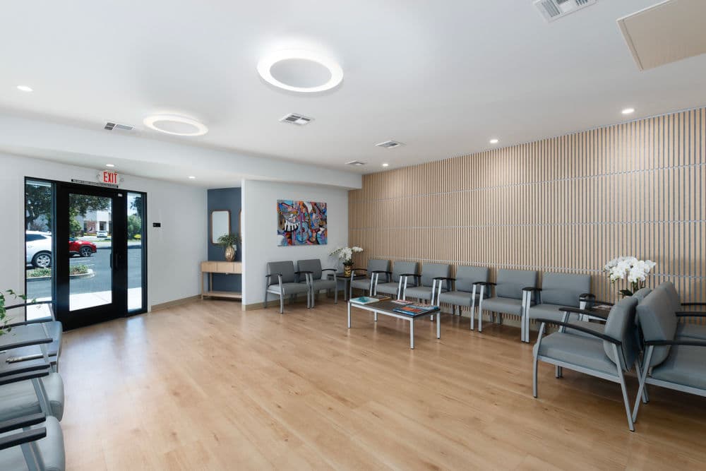 Modern waiting room with gray chairs, wooden floors, and natural light from large windows.