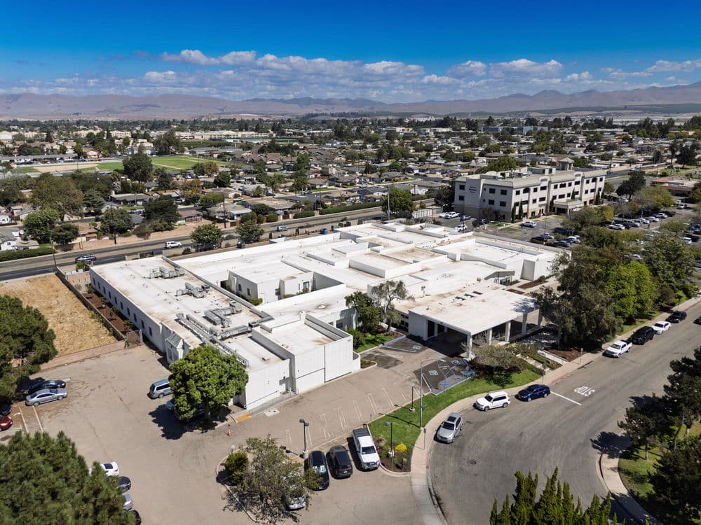 Aerial view of a large commercial building surrounded by parking and residential areas.