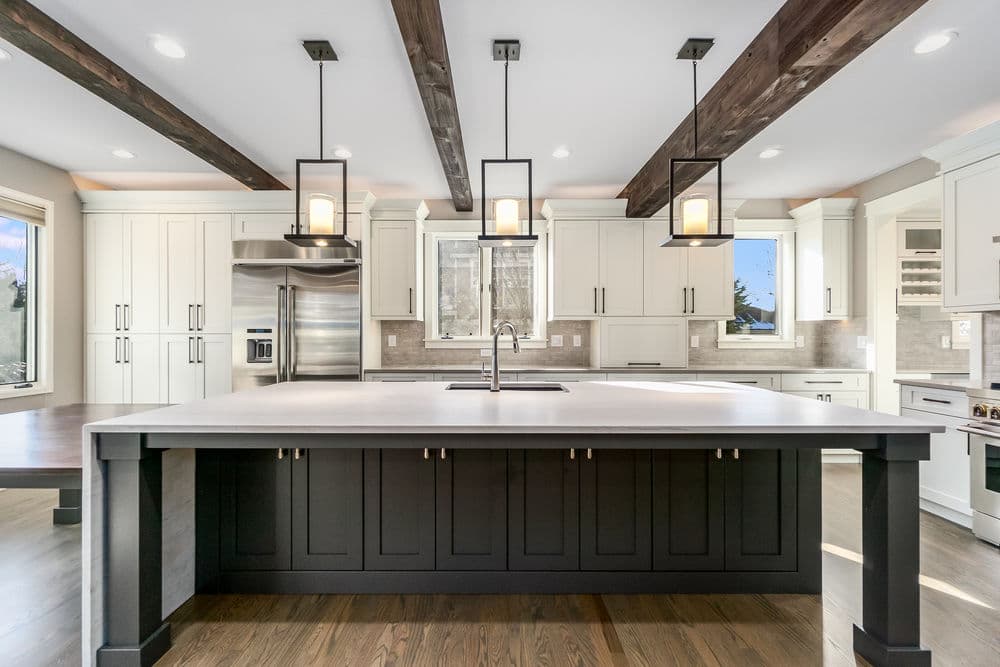 Modern kitchen featuring a central island with black cabinetry, pendant lights, and wooden beams.